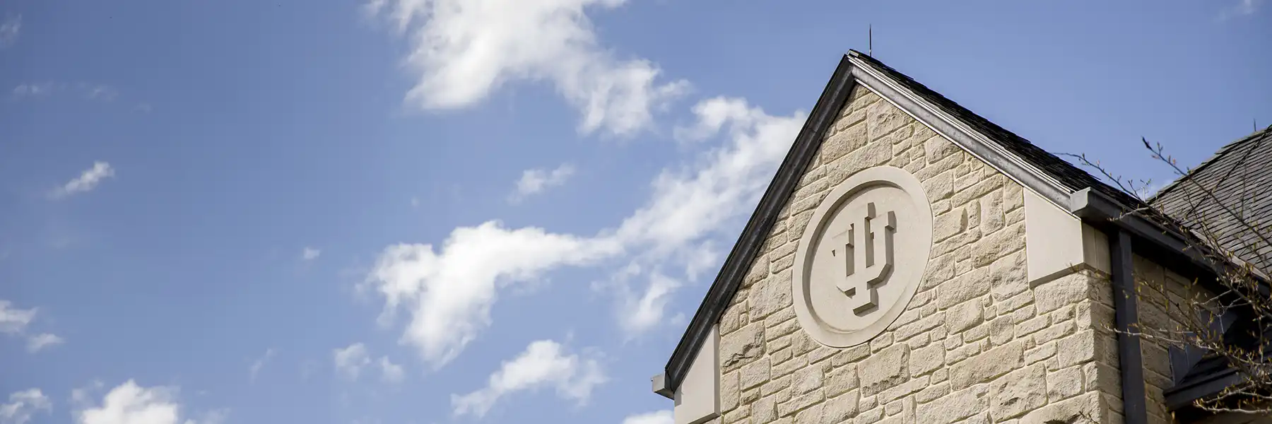 A limestone trident adorns the side of the IUB Hutton Honors College on a spring day.