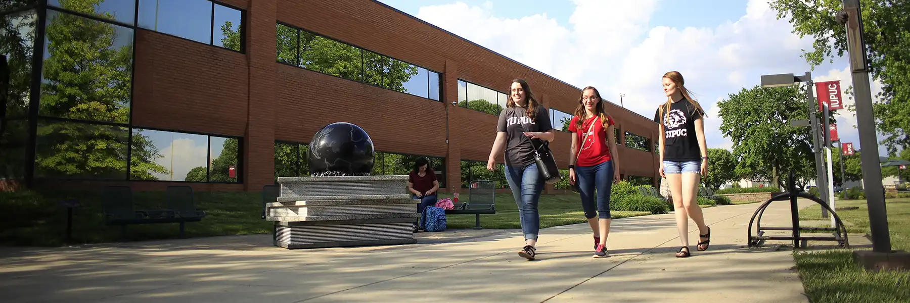 3 students walk along an IU Columbus campus sidewalk on a sunny day.