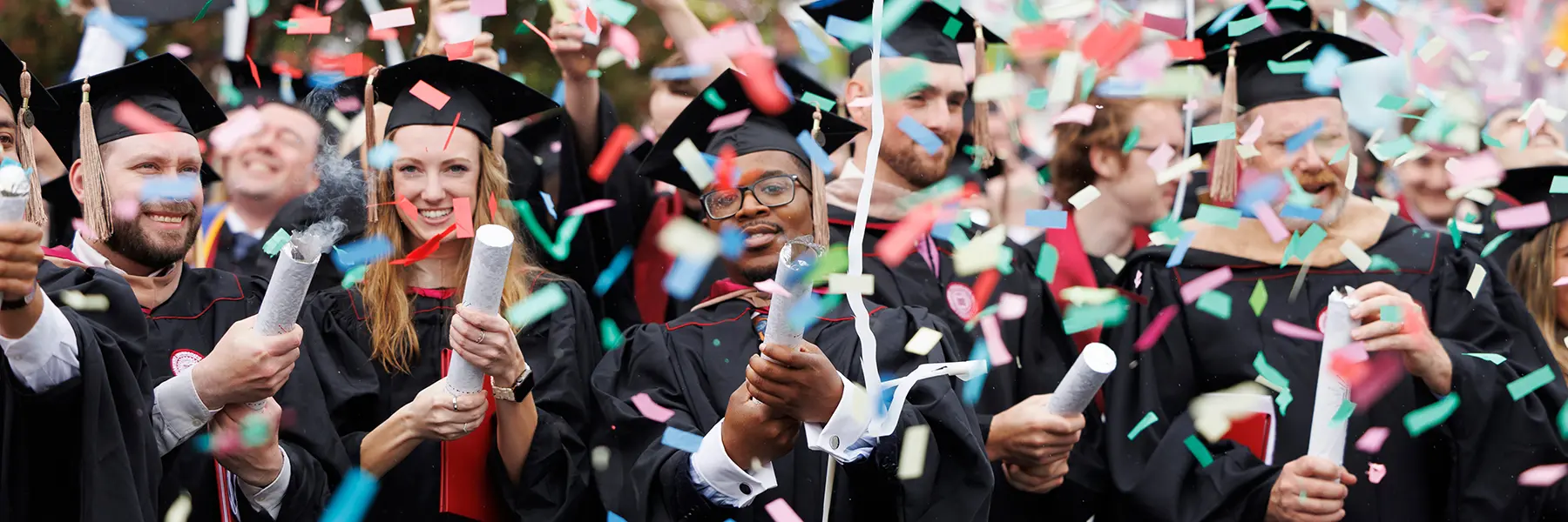 Graduates in regalia pull confetti poppers at IU Southeast graduation.