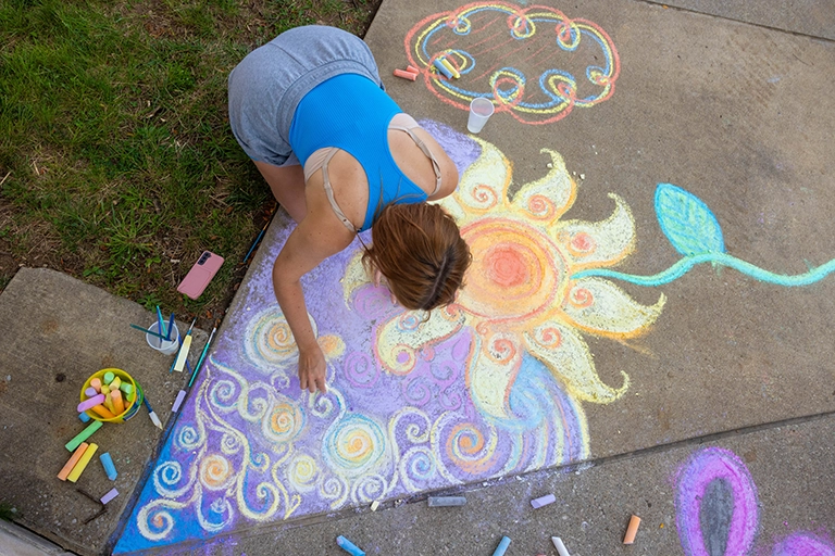 A student makes a detailed chalk drawing on the sidewalk outside Teter Quadrangle on the IUB campus.