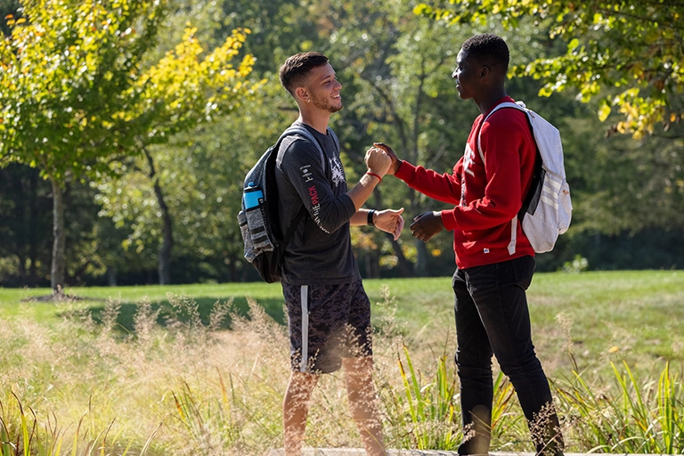 Two students clasp hands in greeting in the central green space on the IU East campus.